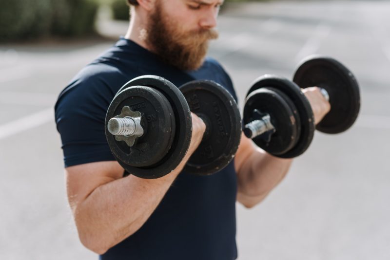 A fit young man, who is holding two weights and is doing arm training