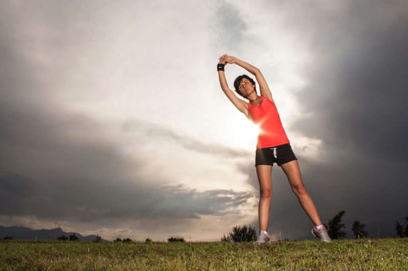 woman out in a field stretching and getting ready to work out. She looks healthy and focused.